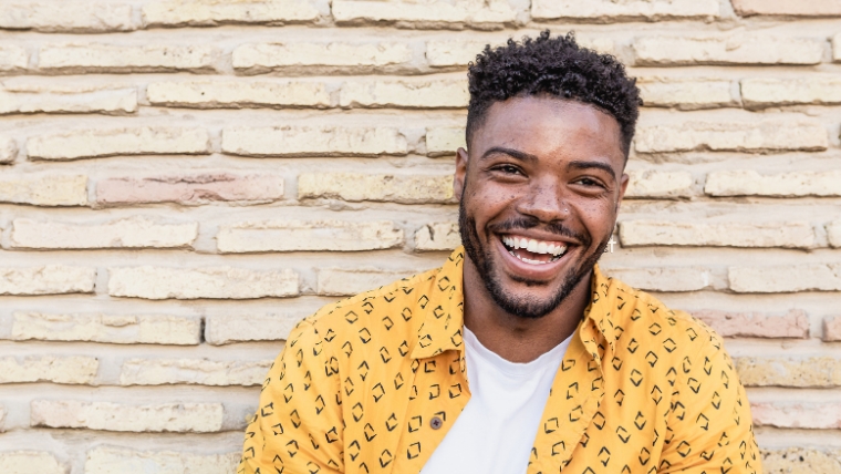 Smiling black man standing in front of a beige brick wall | The Life-Changing Benefits of Combining Medication and Therapy | Mindful Health Solutions