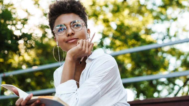 Black women with a notebook holding her chin in her hand while sitting on a park bench | The Pros and Cons of Transcranial Magnetic Stimulation (TMS) for Depression |