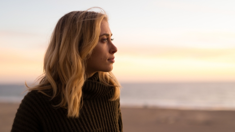 Woman on beach looking off into the distance with a neutral expression | How to Overcome Depression 4 Actionable Steps | Mindful Health Solutions