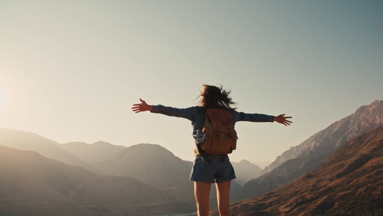 Female person standing on top of mountain and looking out at the view with hands raised victoriously | Reimagine OCD Treatment with TMS A Breakthrough You Should Know About | Mindful Health Solutions
