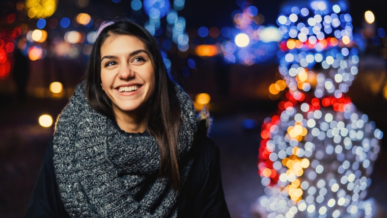 A happy young woman outside at night with Christmas lights behind her | 10 Proven Strategies to Manage Social Anxiety During the Holidays | Mindful Health Solutions
