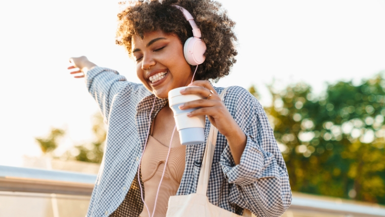 A happy woman with headphones and coffee dancing outside | Get Personalized Mental Health Care and Finally Overcome Your Depression | Mindful Health Solutions