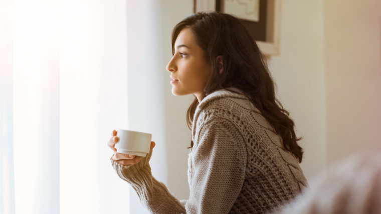 Woman drinking tea on bed thinking seriously | Accelerated TMS vs. Traditional TMS Which One Makes Sense for You | Mindful Health Solutions