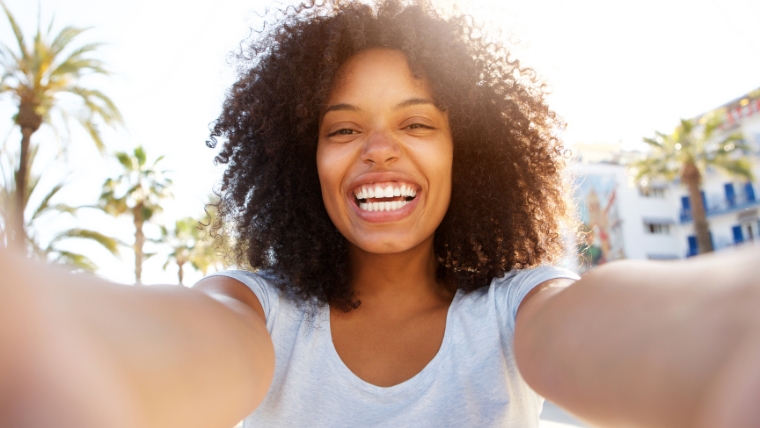 A woman taking a selfie with a big smile in front of palm trees | How Fast Does Esketamine Relieve Depression Compared to Antidepressants? | Mindful Health Solutions