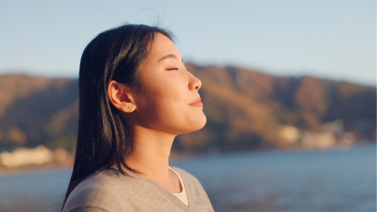 Woman by the mountains and a lake breathing in fresh air with sun on her face | Let's Break Down These 5 Myths About Ketamine Infusion Therapy | Mindful Health Solutions