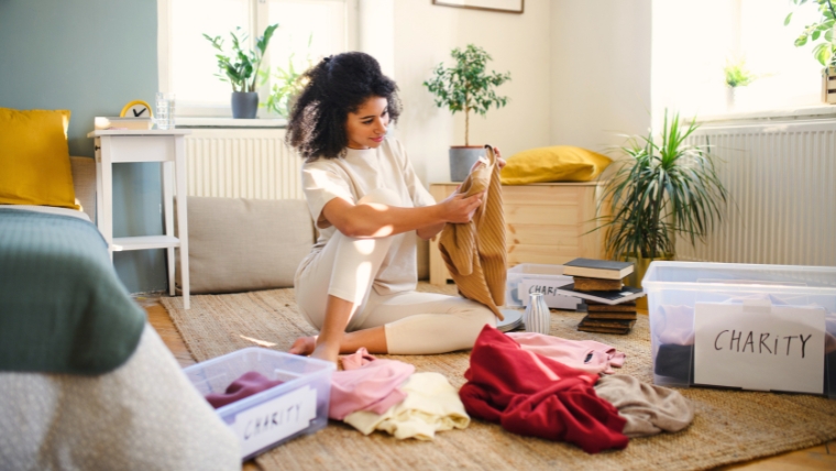 A person is sitting on the floor of their bedroom organizing their clothes to see which can be donated to charity | Declutter Your Home, Declutter Your Mind The Path to Mental Clarity | Mindful Health Solutions