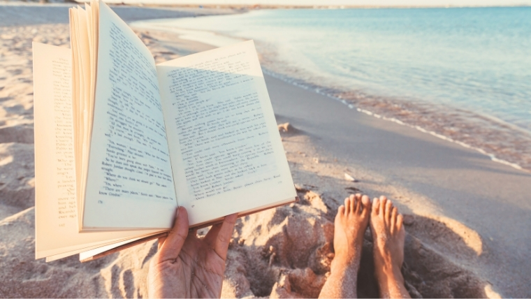 A person reading a book on the beach with their feet in the sand | Find Hope and Relief from Depression Through the Magic of Reading | Mindful Health Solutions