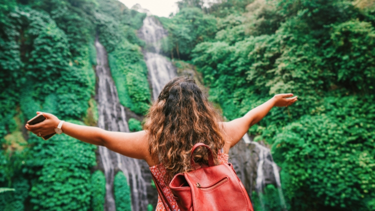 Woman facing a waterfall with a backpack on and her arms wide open | Say Goodbye to Travel Anxiety 8 Simple Ways To Have a Stress-Free Trip | Mindful Health Solutions