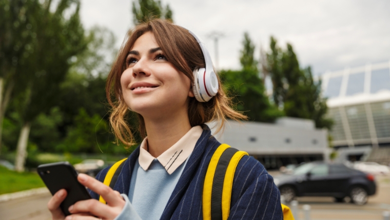 Professional woman with headphones on who is tilting her head up toward the sky with a smile on her face | 7 Ways Music and Podcasts Effectively Soothe Anxiety | Mindful Health Solutions