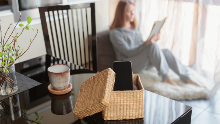 A phone sitting in a basket while a woman is reading | Digital Detox How To Reclaim Control of Your Screen Time and Boost Happiness | Mindful Health Solutions