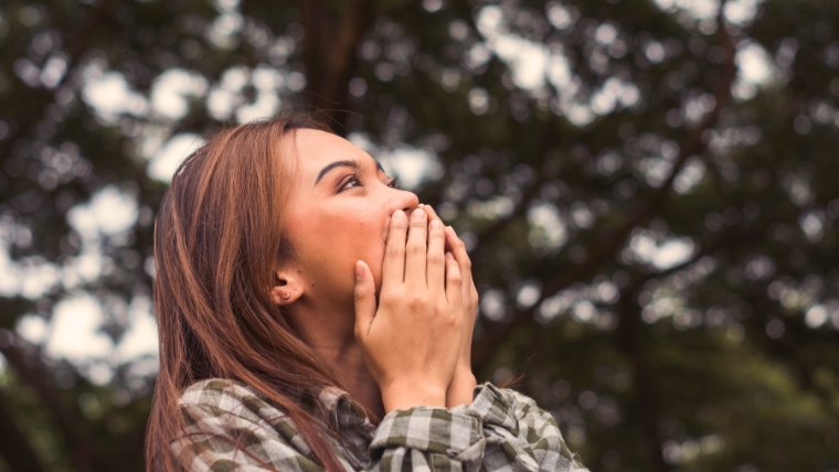Woman standing outside with her hands over her mouth, looking happy and relieved | How To Break Free from Negative Self-Talk and Improve Your Mental Health | Mindful Health Solutions